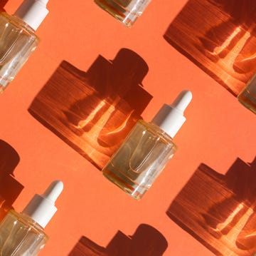 pattern made with glass bottle with cosmetic liquid on bright orange background with shadow and light reflections flat lay style and close up