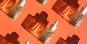 pattern made with glass bottle with cosmetic liquid on bright orange background with shadow and light reflections flat lay style and close up