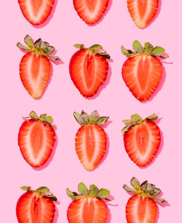 pattern of rows of fresh halved strawberries lying against pink background