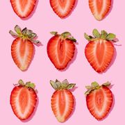 pattern of rows of fresh halved strawberries lying against pink background