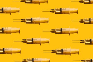 pattern of syringes with a vaccine on yellow background concept of medical treatment or vaccination