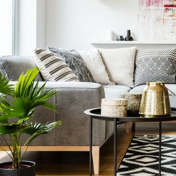 Patterned pillows on grey corner sofa in living room interior with table and painting. Real photo