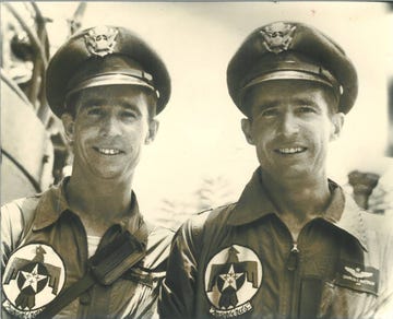two men in air force uniforms and hats smile as they stand together for a photo