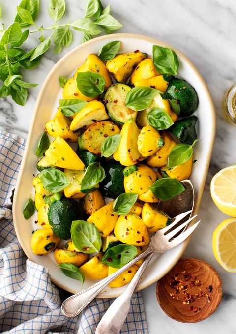 sautéed patty pan squash in an oval serving dish with fresh basil and red pepper flakes