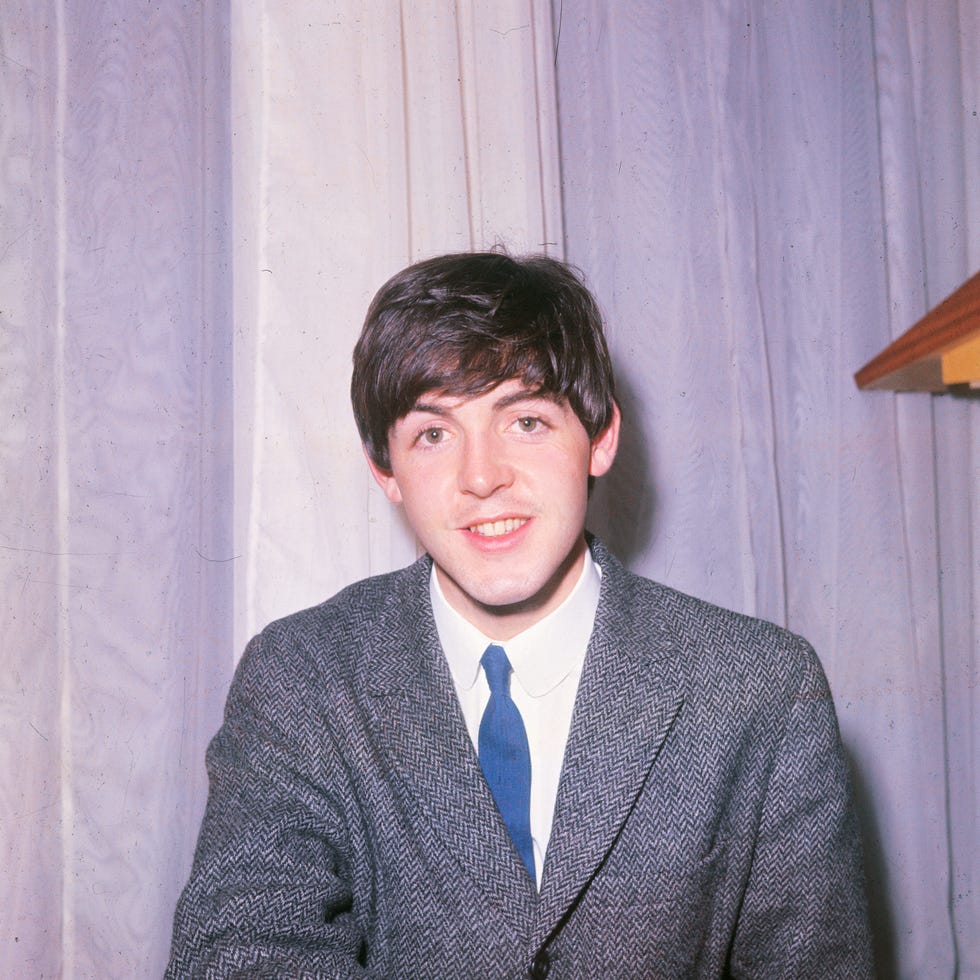 paul mccartney wearing a grey suit jacket and blue tie seated in front of a curtain