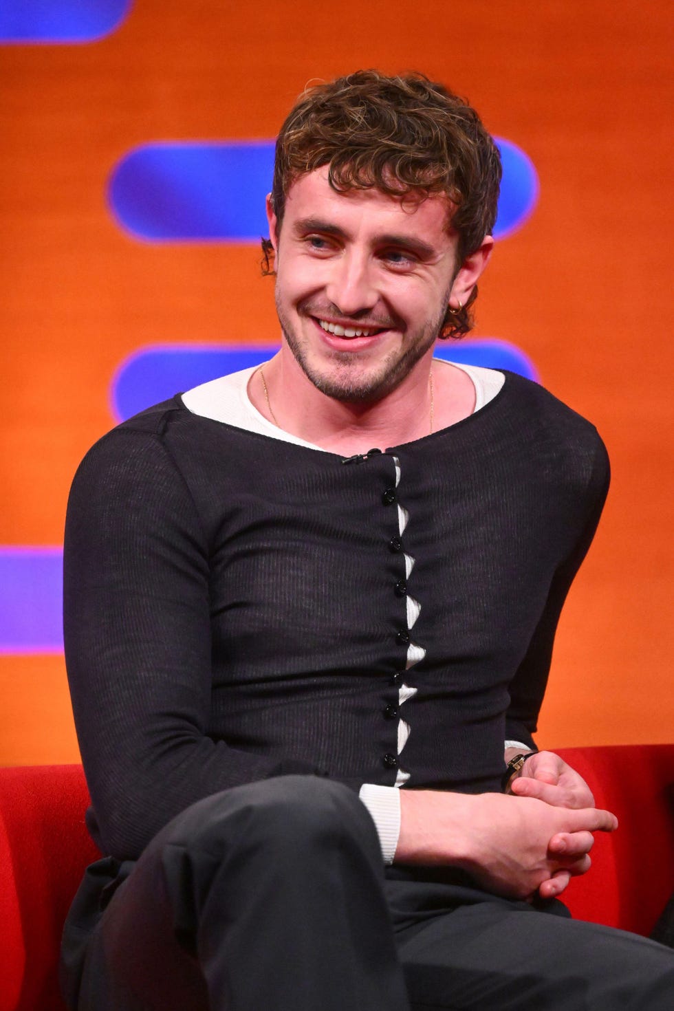 a person seated on a red sofa wearing a black buttonup shirt and black pants