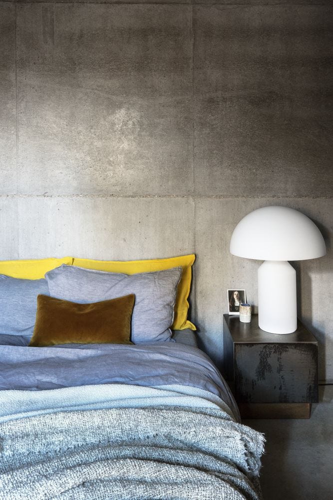 Bed with layered textured blue bedding and yellow accent pillowcases against concrete wall