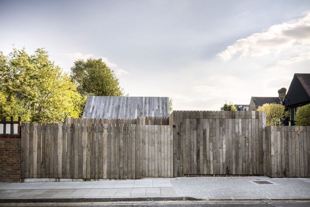 Street with wooden fence; wooden structure, roof, trees and sky appear behind fence