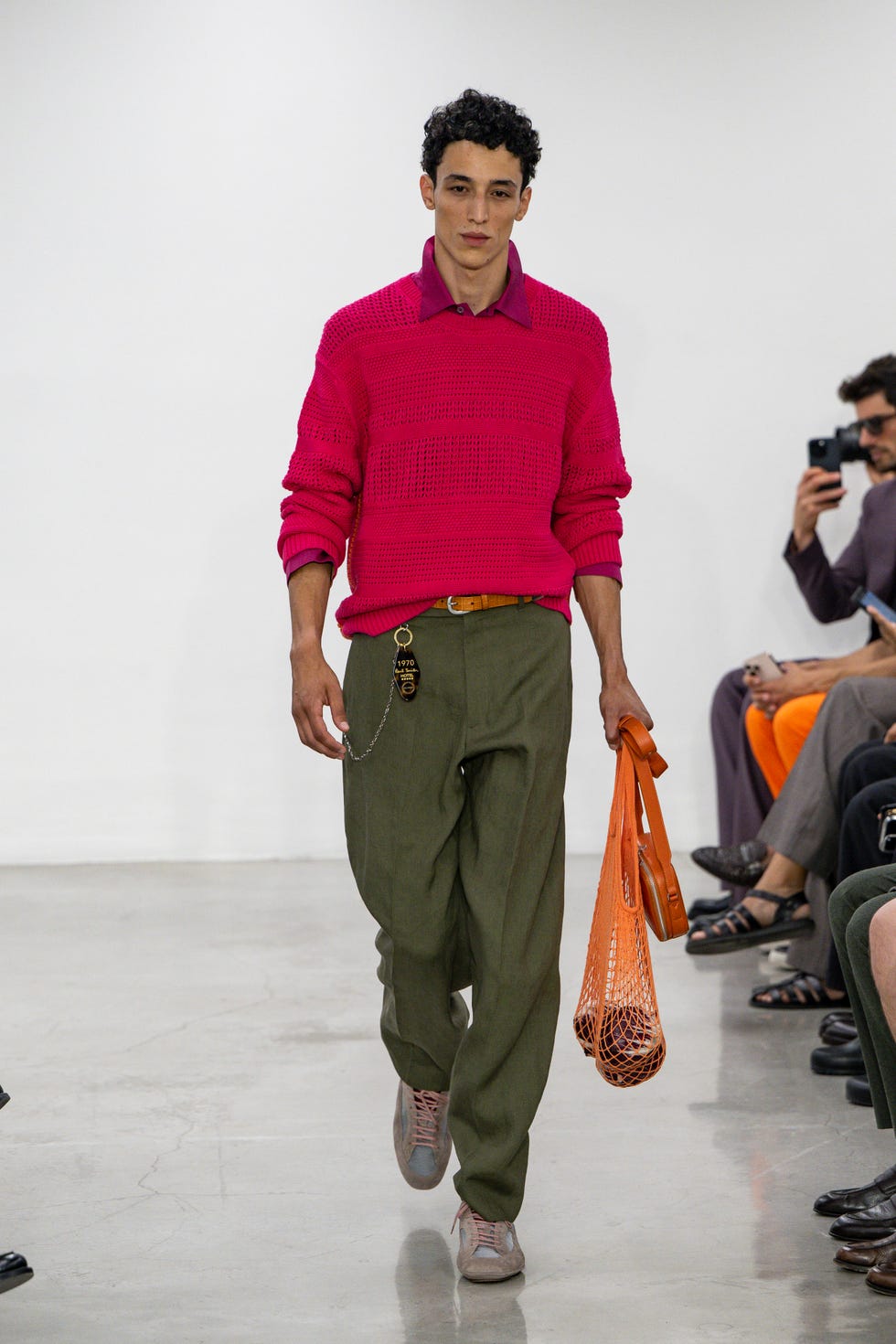 a male model showcasing a vibrant pink sweater olive green pants and an orange tote bag