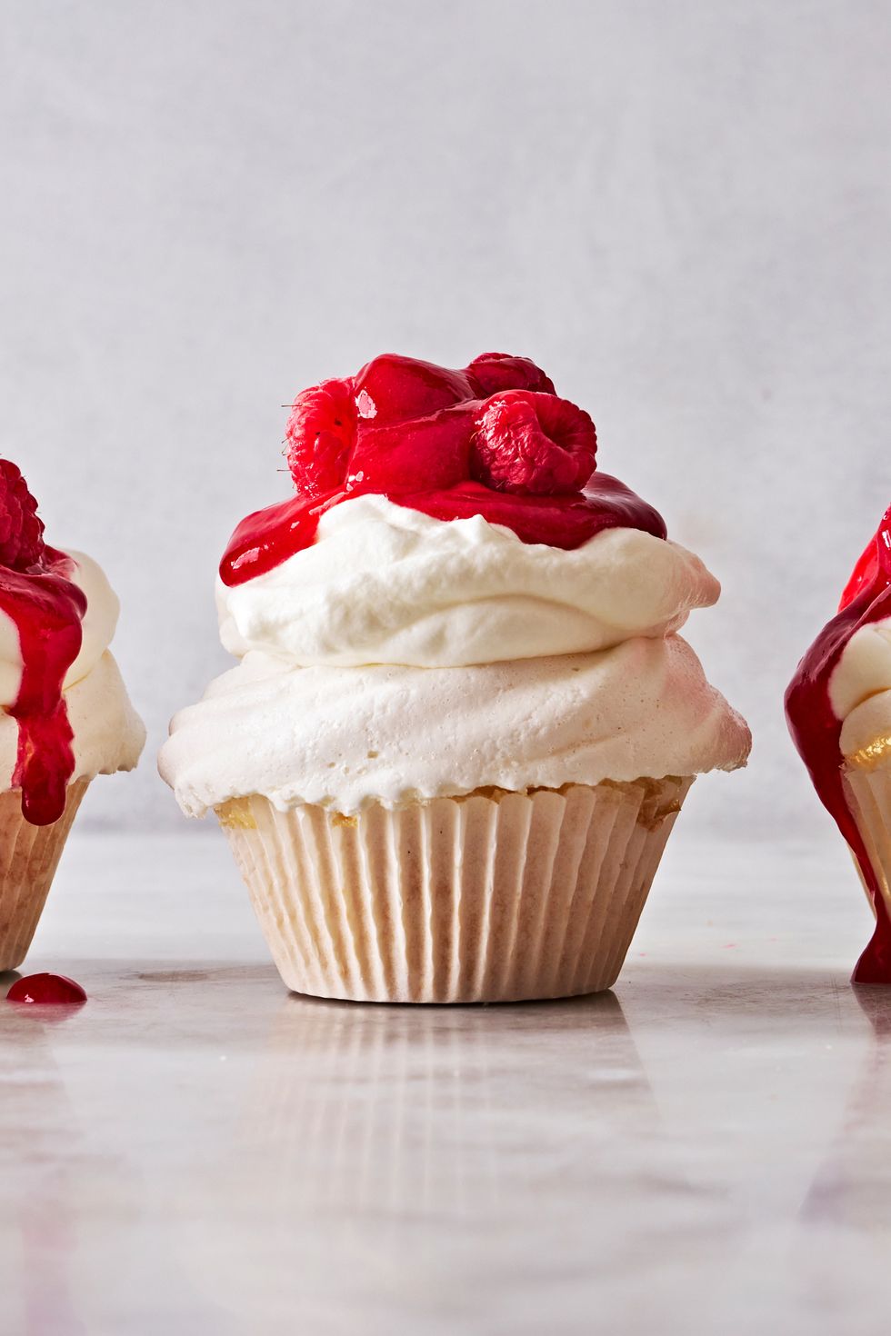 pavlova cupcakes topped with whipped cream and raspberry sauce