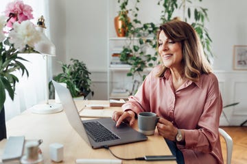 beautiful smiling mature woman sitting in the comfot of her home office and working, social distancing concept