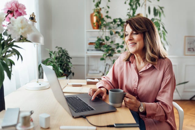 beautiful smiling mature woman sitting in the comfot of her home office and working, social distancing concept