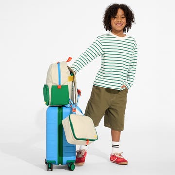 New Away luggage and backpacks plus lunchboxes child standing next to colorful luggage and backpacks from the brand away