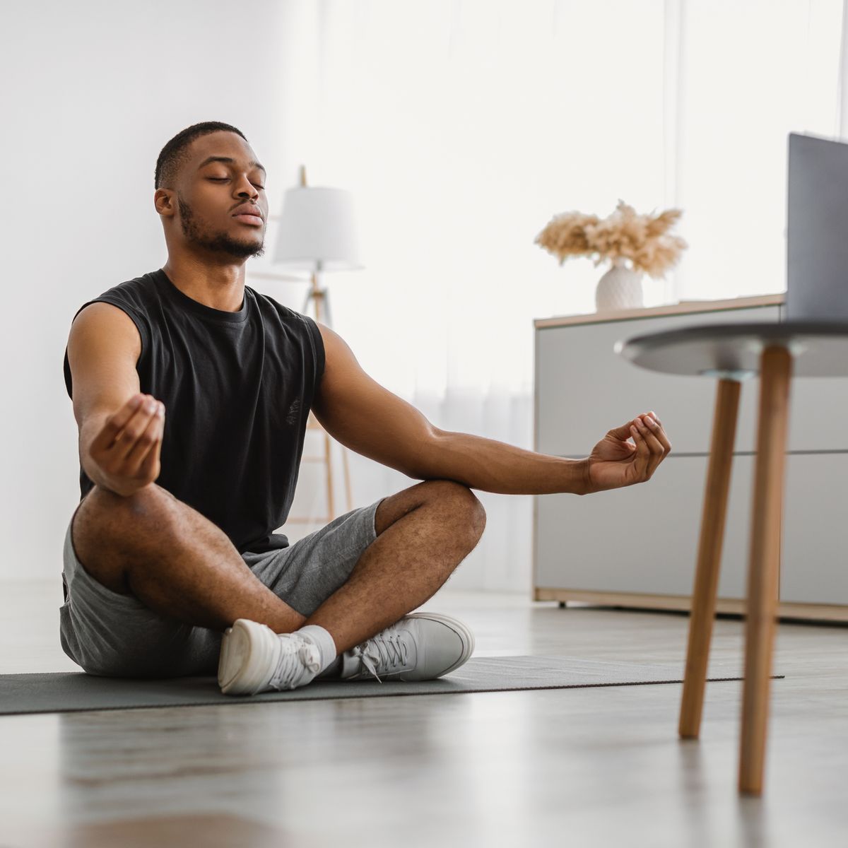 peaceful african american guy meditating at computer at home