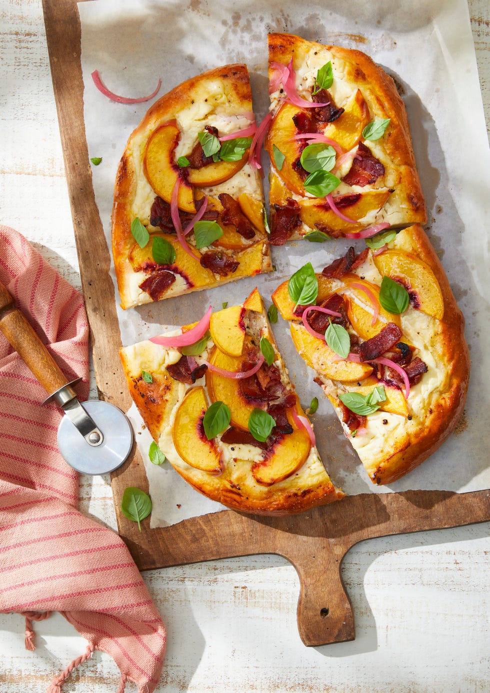 a peach and bacon pizza with basil on a cutting board