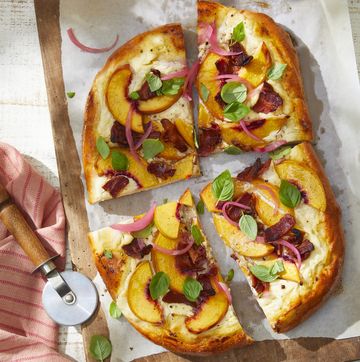 a peach and bacon pizza with basil on a cutting board