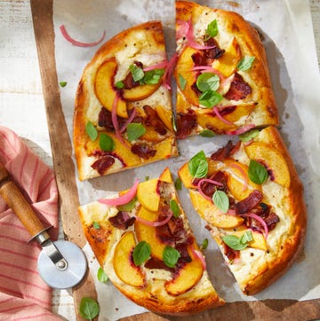 a peach and bacon pizza with basil on a cutting board