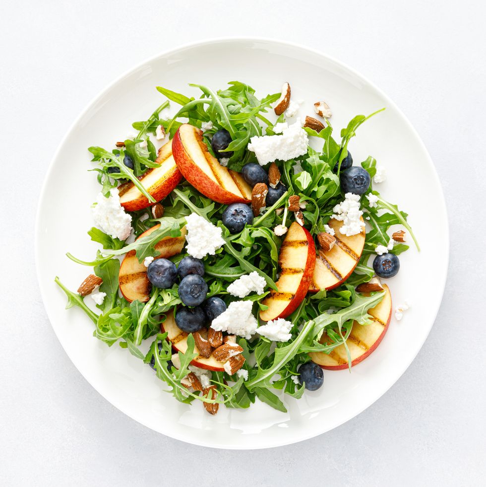 peach, blueberry and arugula fresh fruit salad with cheese and almond nuts, top view