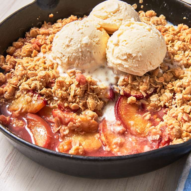 peach crisp topped with oat crumble and vanilla ice cream in a black cast iron baking dish