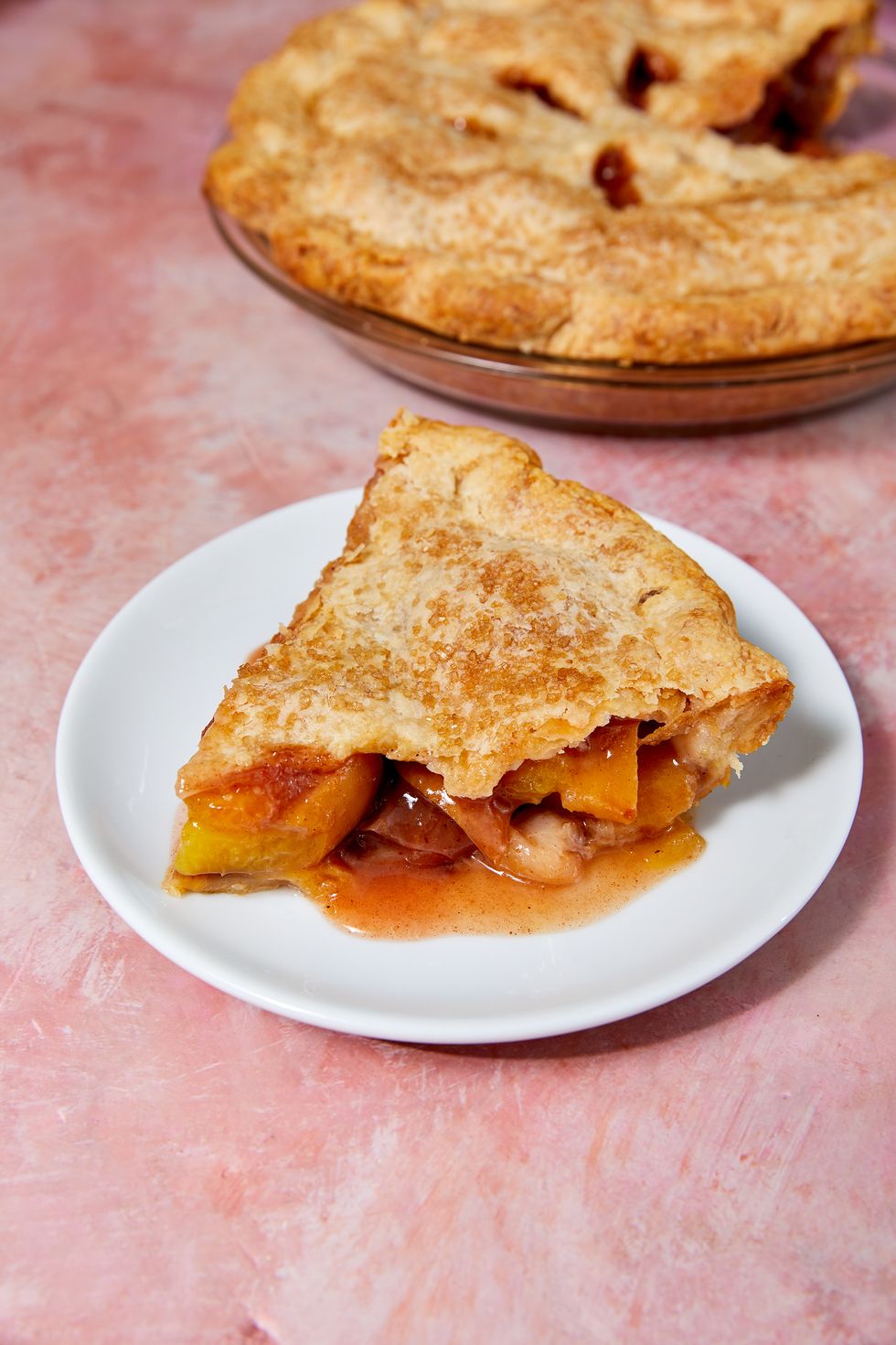 slice of bourbon peach pie on a white plate on a pink background