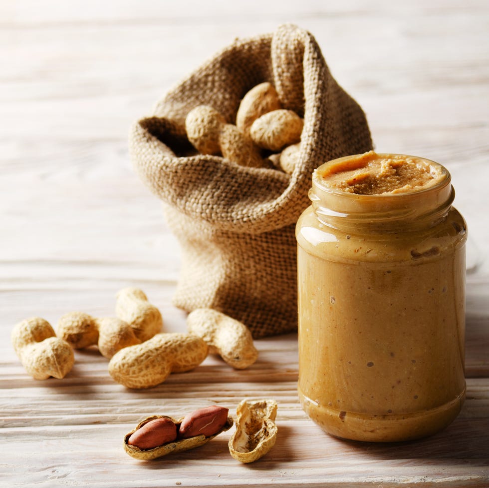 low angle view at glass mason jar with peanut butter on white wooden table with burlap sack on backside healthy eating concept