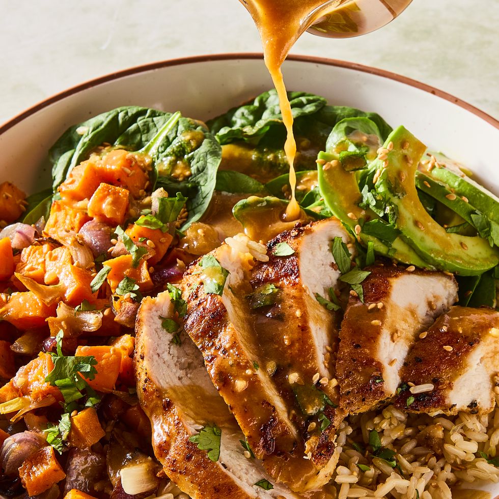 sliced chicken in a grain bowl with sweet potatoes, avocados, spinach and a peanut dressing
