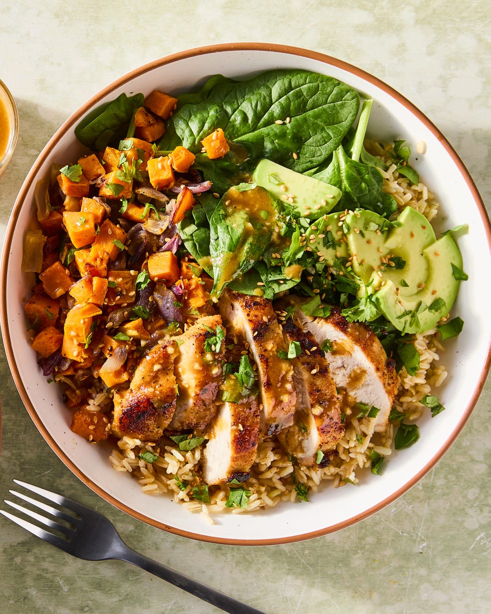 sliced chicken in a grain bowl with sweet potatoes, avocados, spinach and a peanut dressing