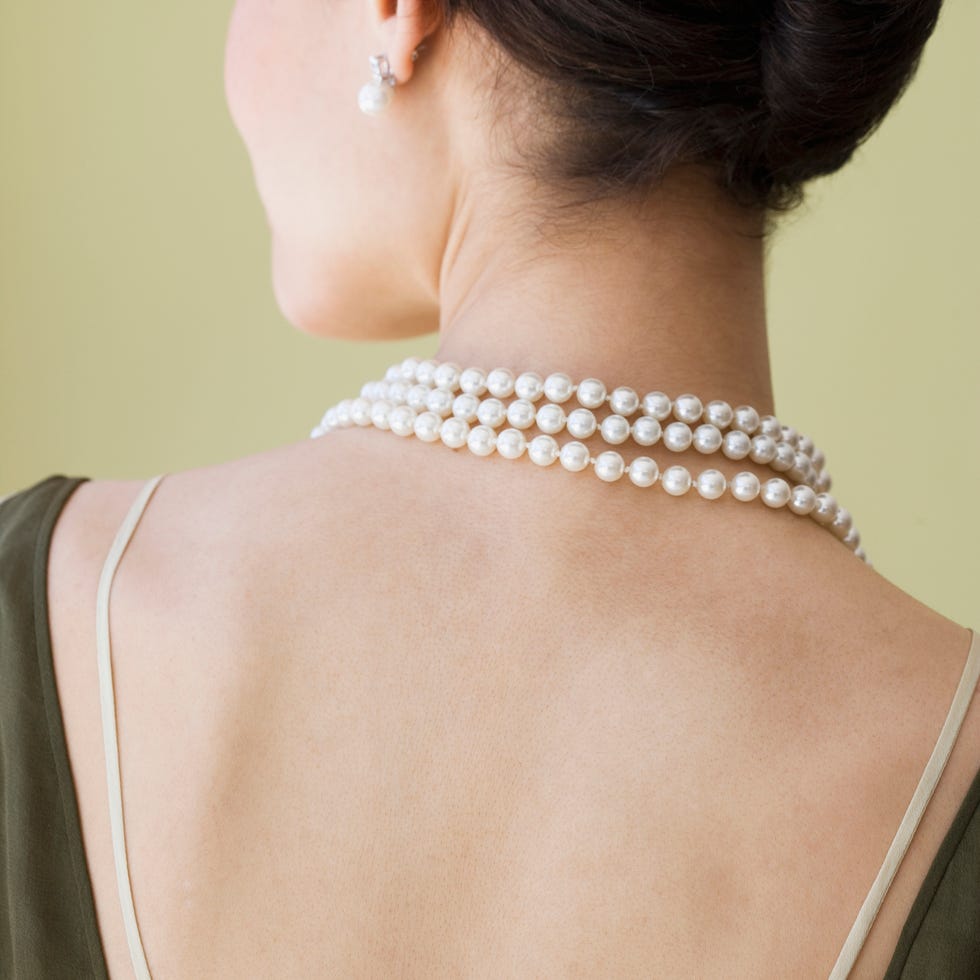 a woman wearing a white pearl necklace and earrings, facing away from the camera