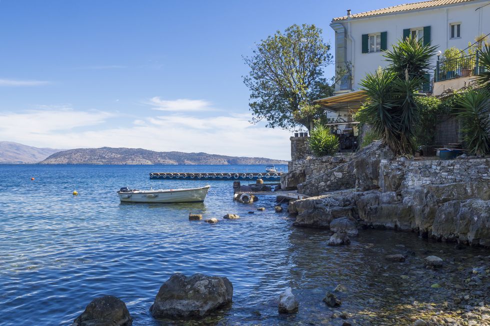 pebble sea shore and the white house in kalami boat and pier at stone quay summer blue sky, corfu greece