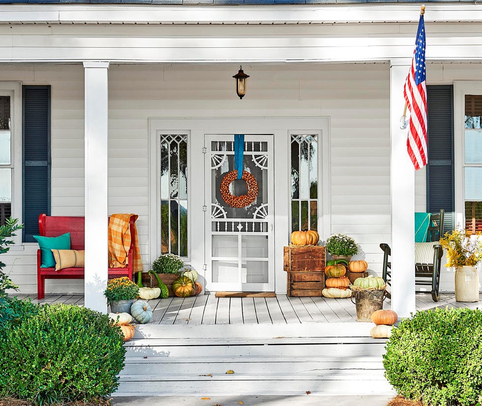 fall porch with pumpkins, a pecan shell wreath, mums, and cozy blankets