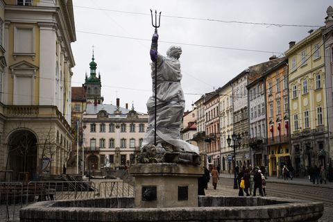 pedestrians walk past a wrapped statue next to the latin cathedral in lviv