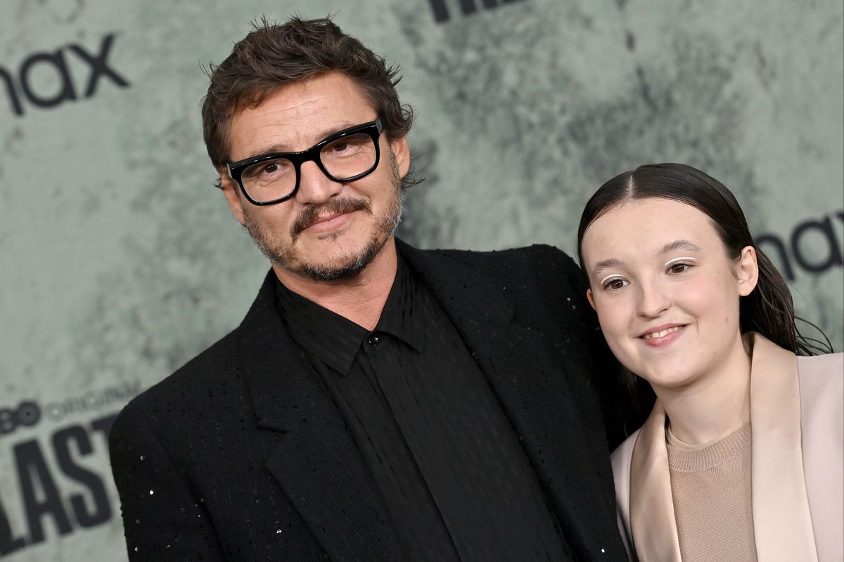 pedro pascal, wearing a black suit and glasses, and bella ramsey, wearing a peach dress suit, smiling for publicity photos