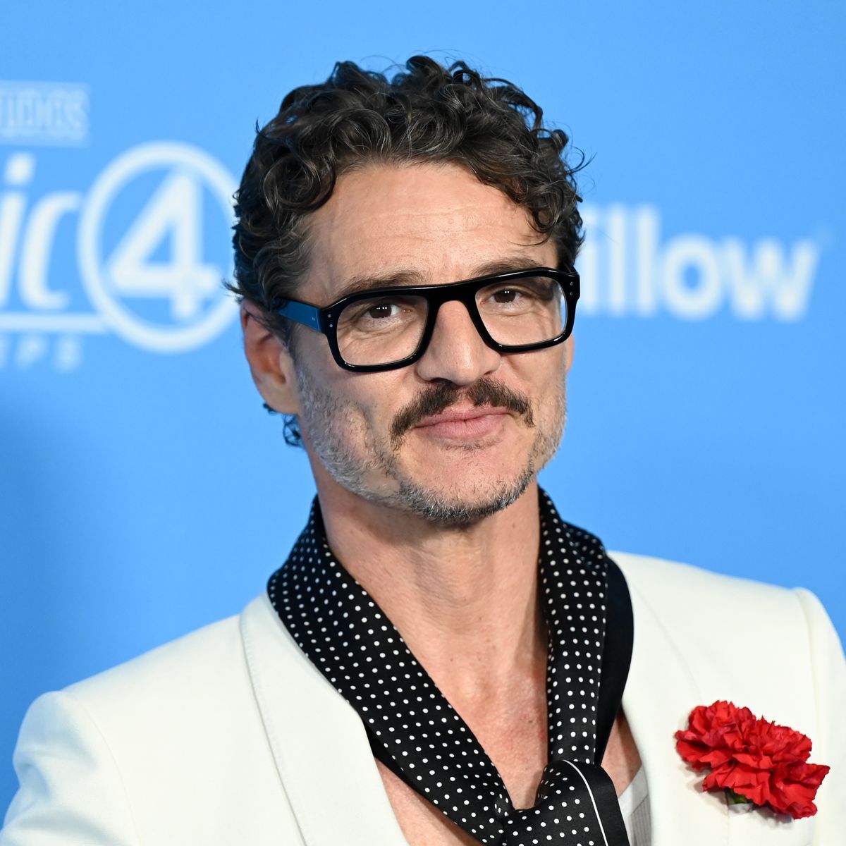 pedro pascal poses wearing white suit jacket and polka dot scarf