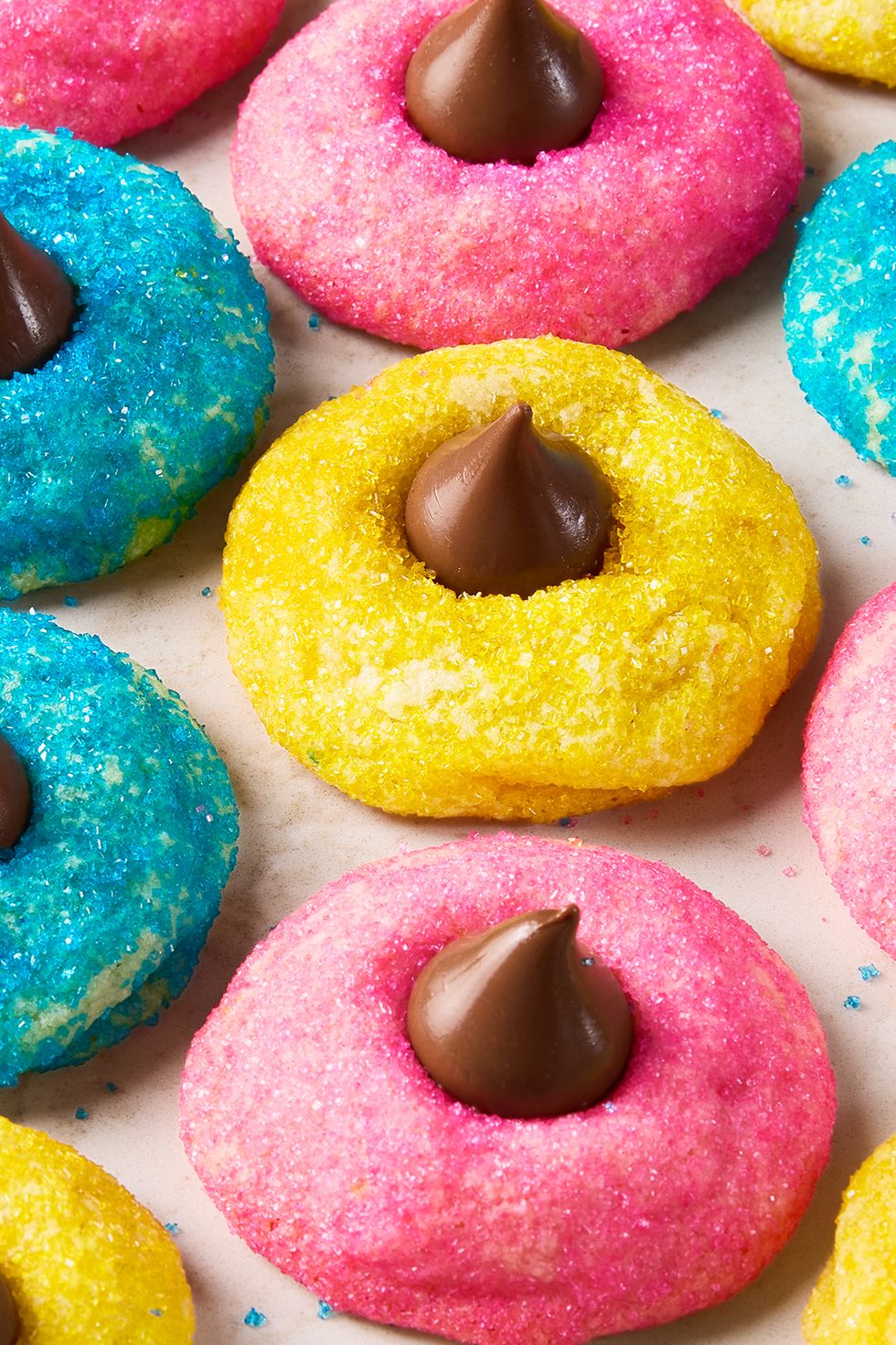 blue pink and yellow dyed cookies with sugar and topped with a hershey kiss