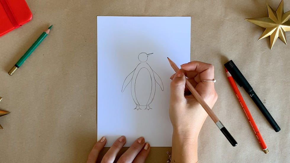 a person drawing a penguin character on a white paper