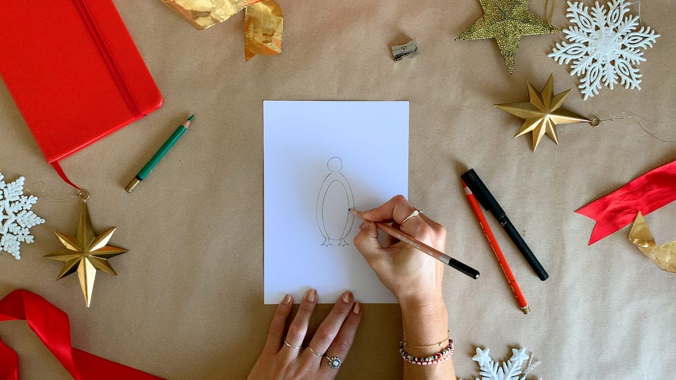 hands of illustrator drawing a penguin on a piece of white paper