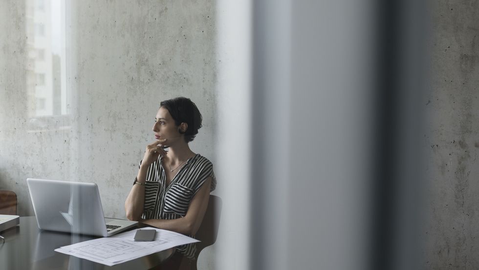 Pensive female architect at laptop looking away in conference room