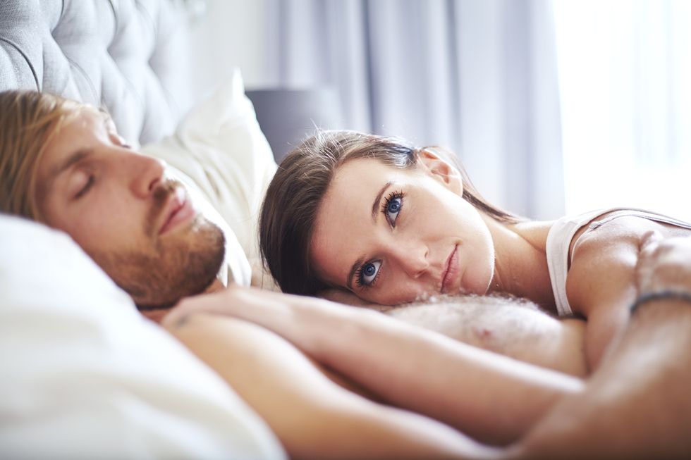 Pensive woman laying on sleeping man on bed