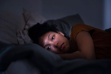 jonge vrouw ligt in bed in het donker met licht aan, ze kijkt bedenkelijk