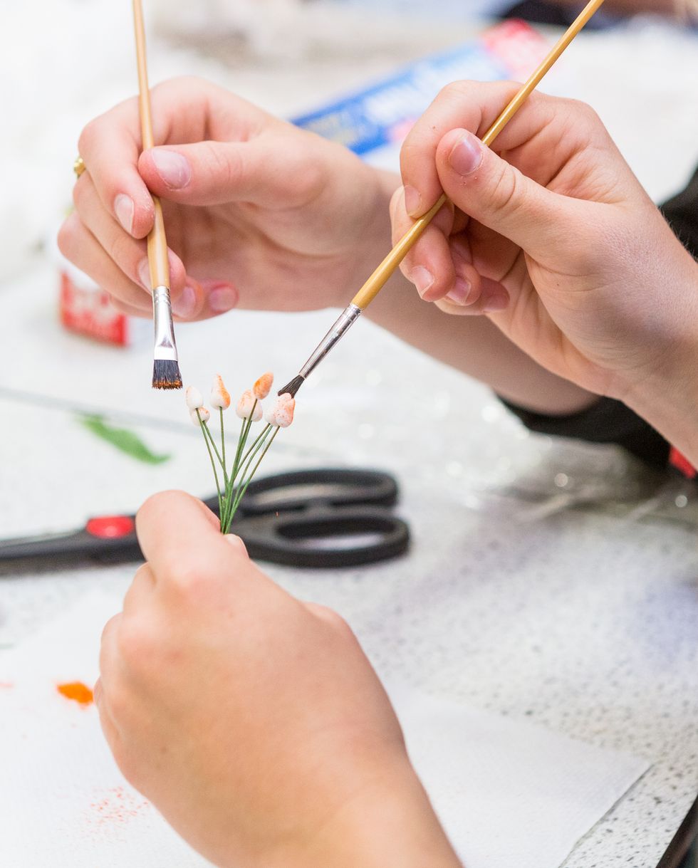 people painting miniature flowers with paint brushes with only hands visible