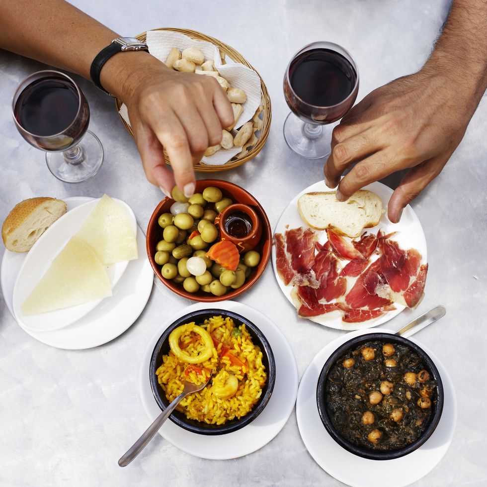 People eating tapas at outdoor restaurant, close-up of hands, overhead view