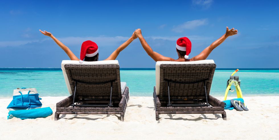 People In Santa Hat Sitting On Lounge Chair At Beach Against Sky