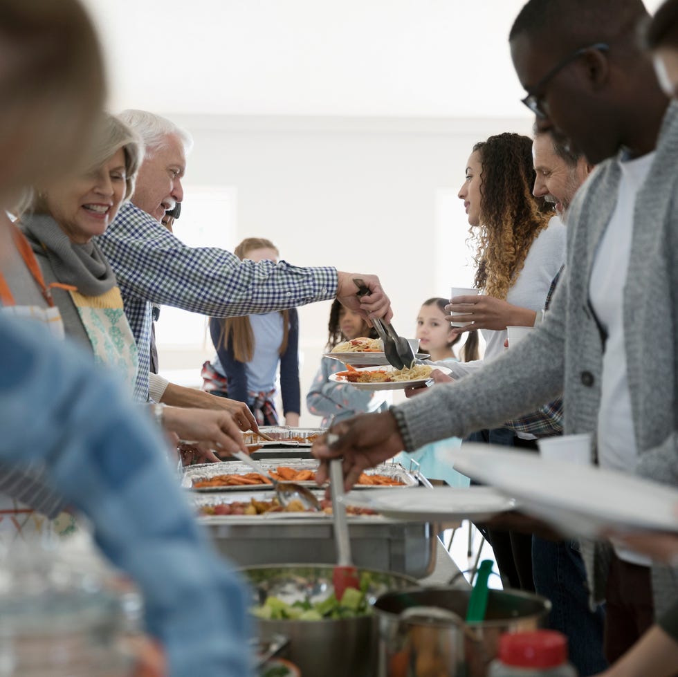 thanksgiving traditions   people serving food at a soup kitchen over a line of aluminum warming trays