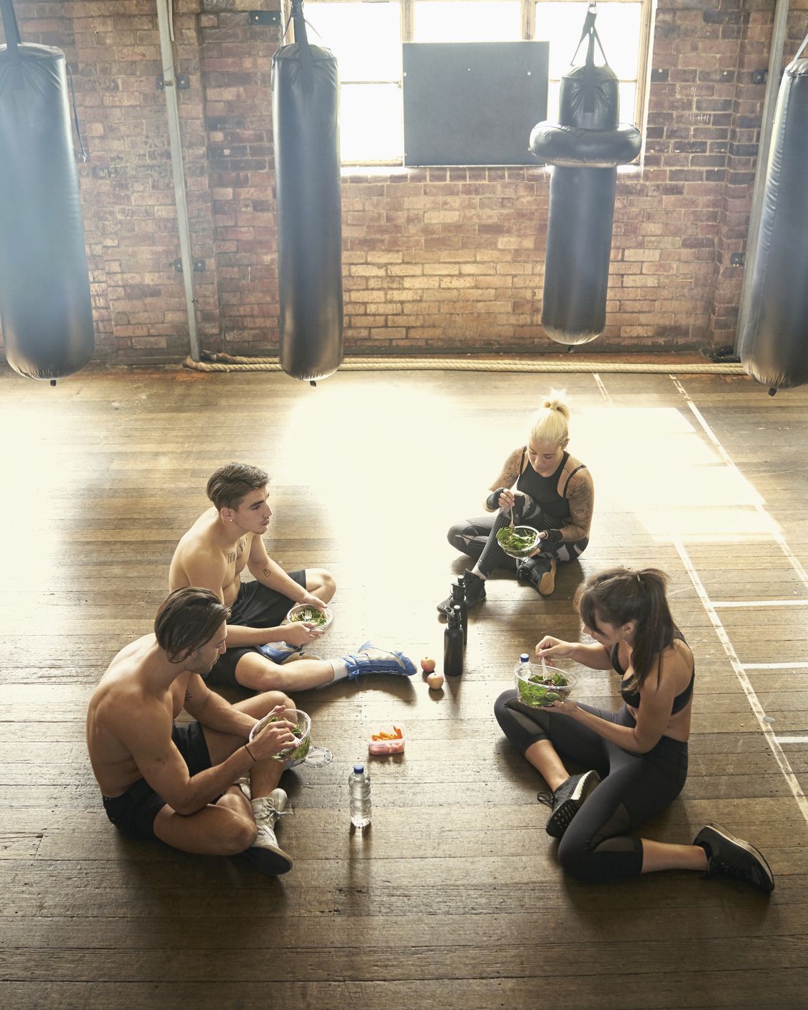 People sitting on floor in gymnasium eating salads