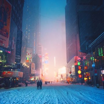 people walking in the streets of times square after they are closed to traffic during a blizzard