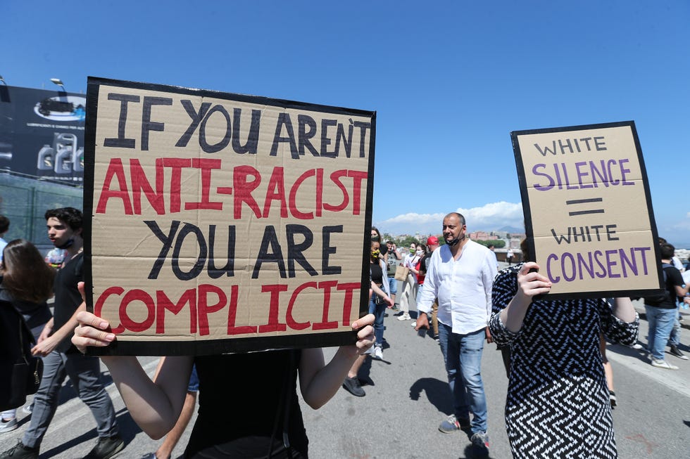 two protestors holding up signs that read 'if you aren't anti racist, you are complicit' and 'white silence equals white consent'