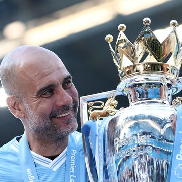 manchester city manager pep guardiola smiles as he holds the premier league trophy