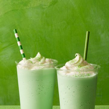 two green shakes with whipped cream on top, against a green background
