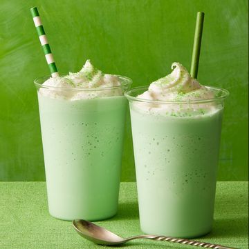 two green shakes with whipped cream on top, against a green background