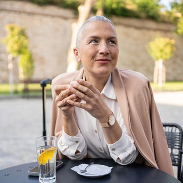 perfume colonia mujer aroma oriental una mujer se toma un café en una terraza. lleva el pelo corto y va vestida con una camisa blanca y una chaqueta de rosa palo de entretiempo